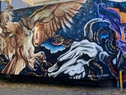 Colorful graffiti mural featuring a large owl with spread wings, a tiger's head, and abstract swirling designs in vibrant blues, purples, and oranges.