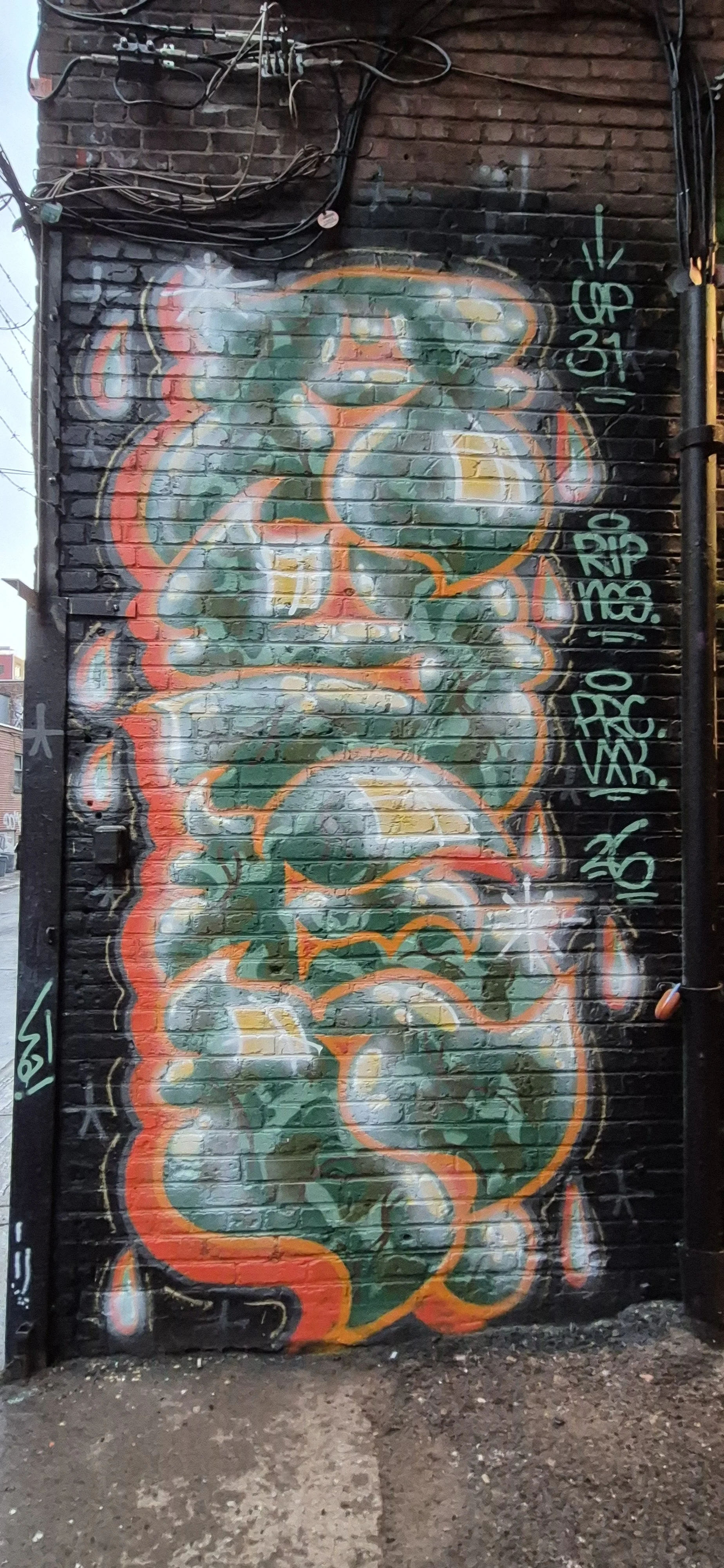 Colorful graffiti art on a brick wall featuring abstract shapes outlined in orange with green and yellow fill, and tags in green on the right side.
