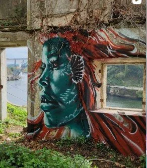 Colorful graffiti mural of a woman's side profile with tribal markings on an exterior wall.