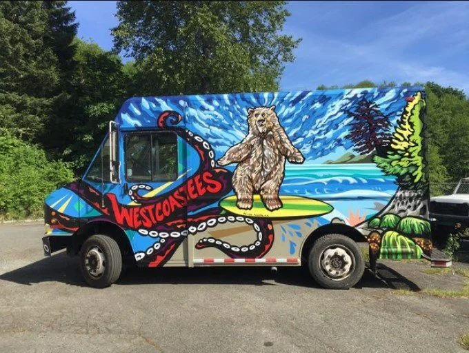 Colorful mural on a food truck featuring a bear on a surfboard, surrounded by water, trees, and ocean waves.