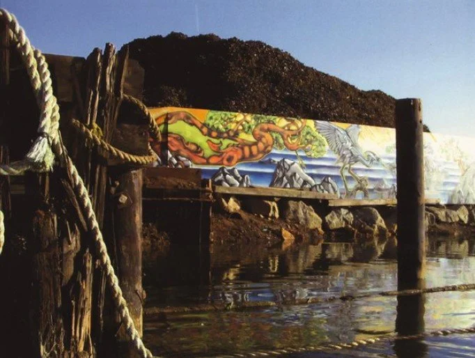 View of a wooden dock with ropes, a colorful mural of a dragon and horses, and a mountain in the background