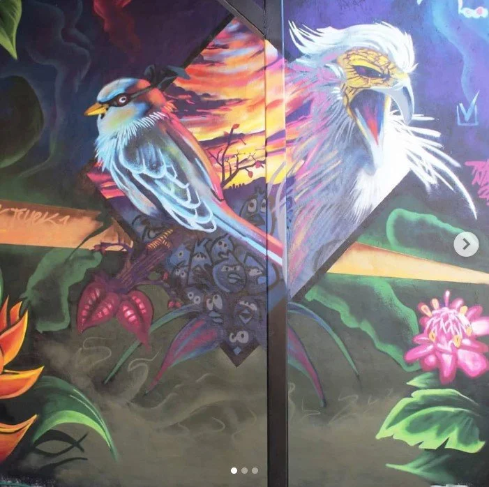 Colorful mural featuring a blue and brown bird on a branch, a large roaring white eagle with a yellow beak, pink flowers, and a sunset background with clouds and trees. Art, street art, painter, mural, graffiti, spray paint, oil paint, montreal, comm