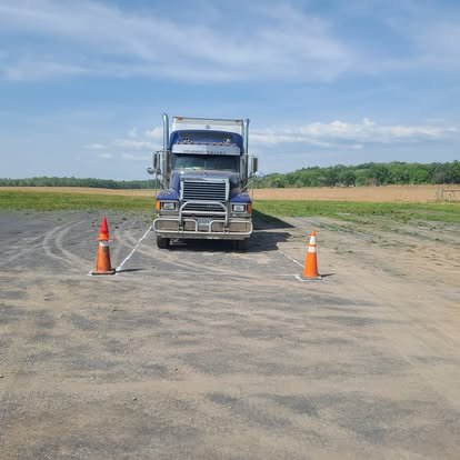 A semi truck parking on a gravel lot, blocked by two orange traffic cones.