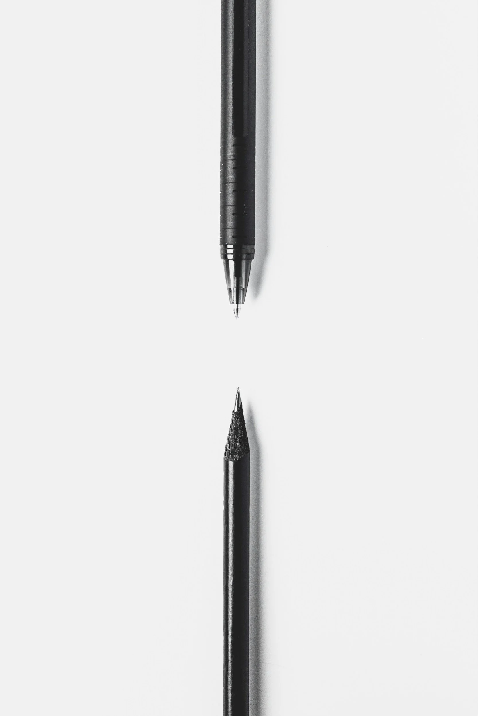 A mechanical pencil, a pen, and a black pencil resting on a white surface with a shadow.