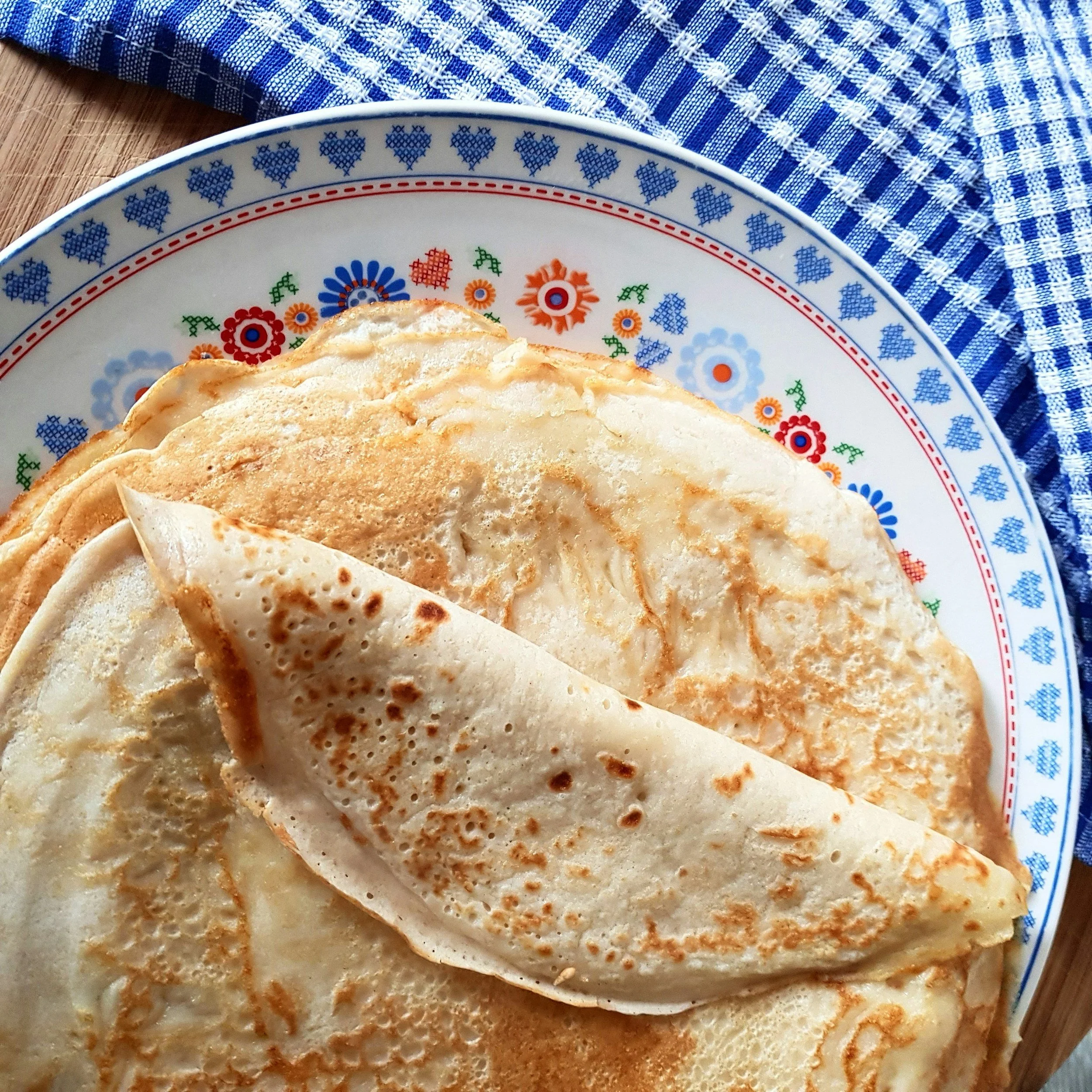 Close-up van een bord met gebakken pannenkoeken, op een blauwe en witte doek ligt op de achtergrond.
