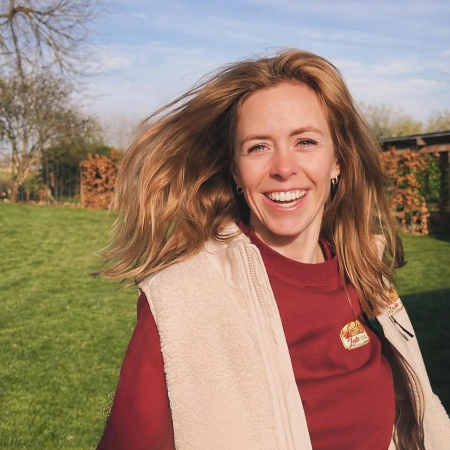 Vrolijke vrouw met lang, lichtbruin haar die in de buitenlucht lacht.