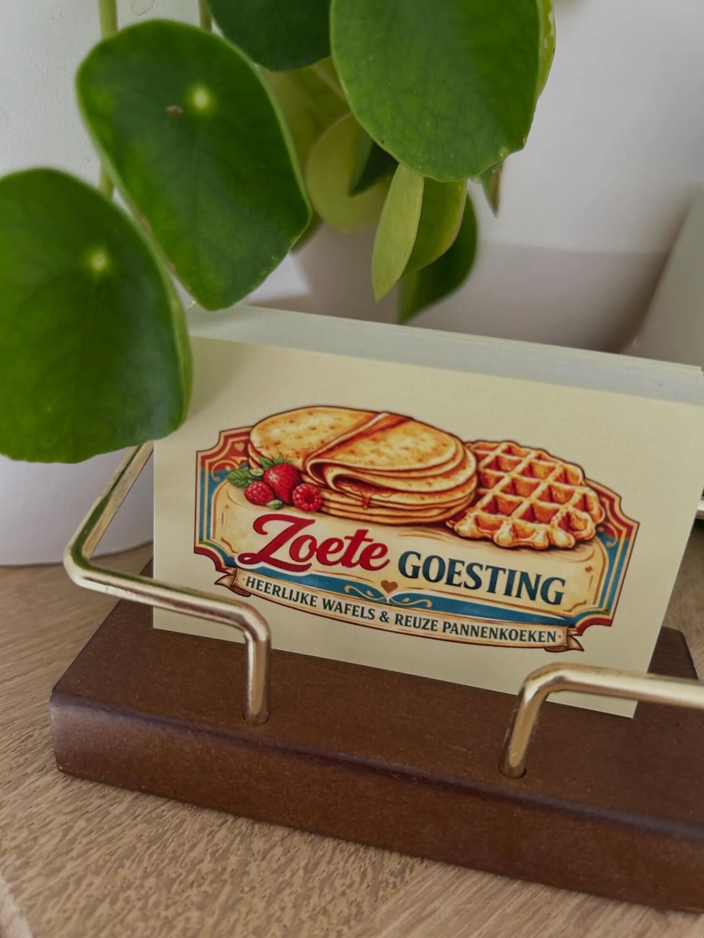 Close-up van een plant met grote groene bladeren naast een bord met de tekst 'Zoete Goesting' en afbeeldingen van wafels en fruit.