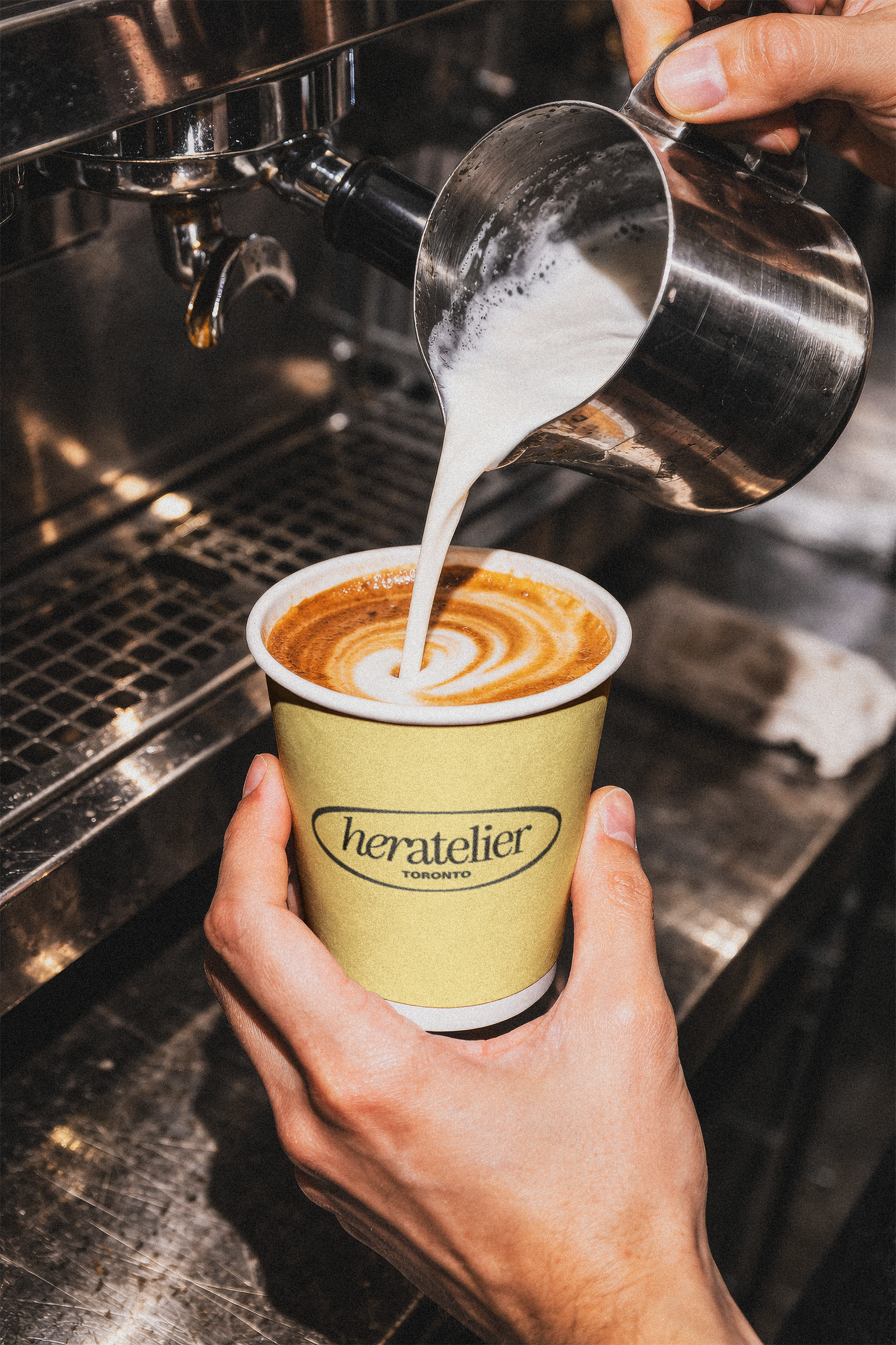 A person is pouring steamed milk into a cup of espresso, creating latte art at a coffee shop.