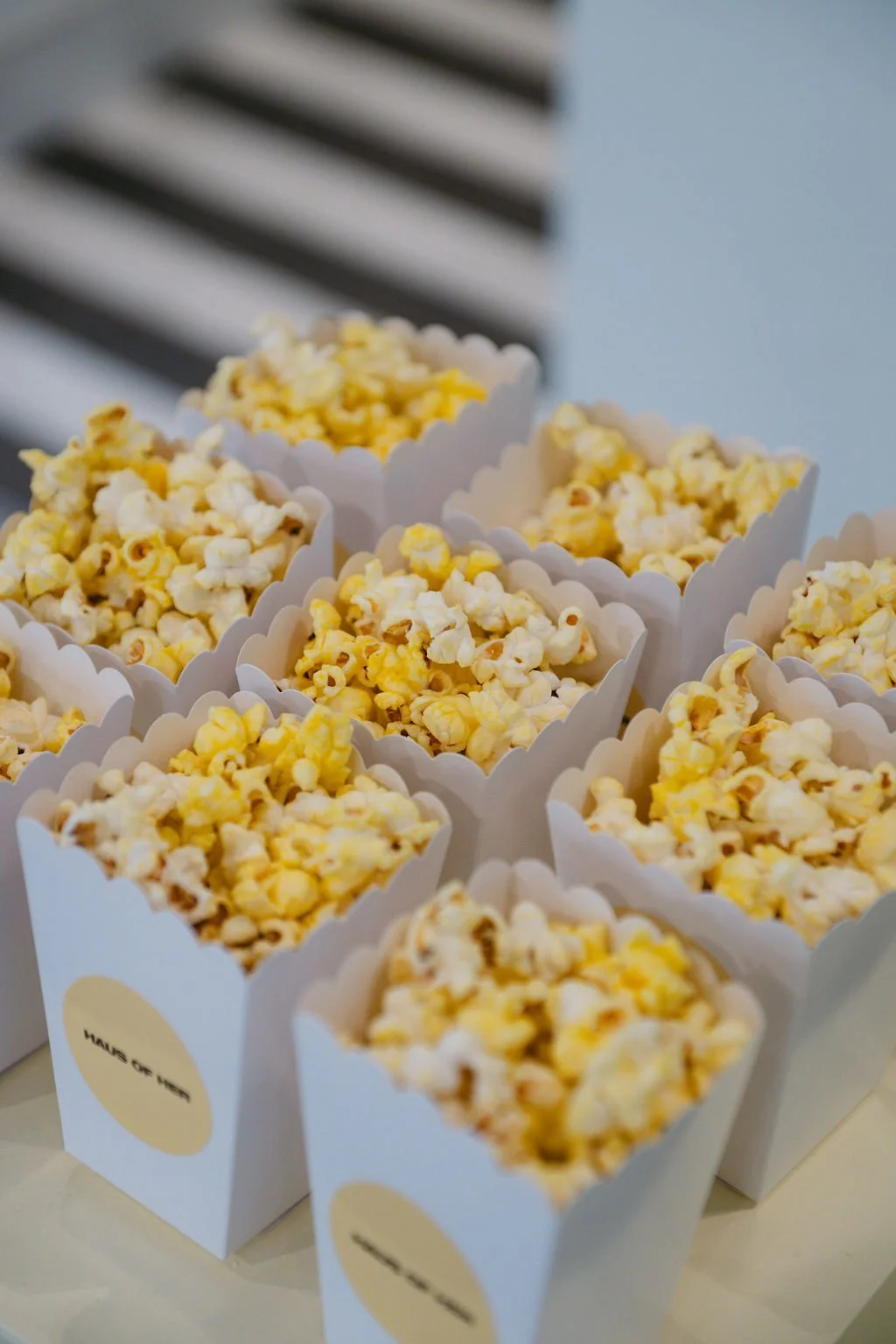 Multiple containers of popcorn inside white paper containers, with a black and white striped surface in the background.