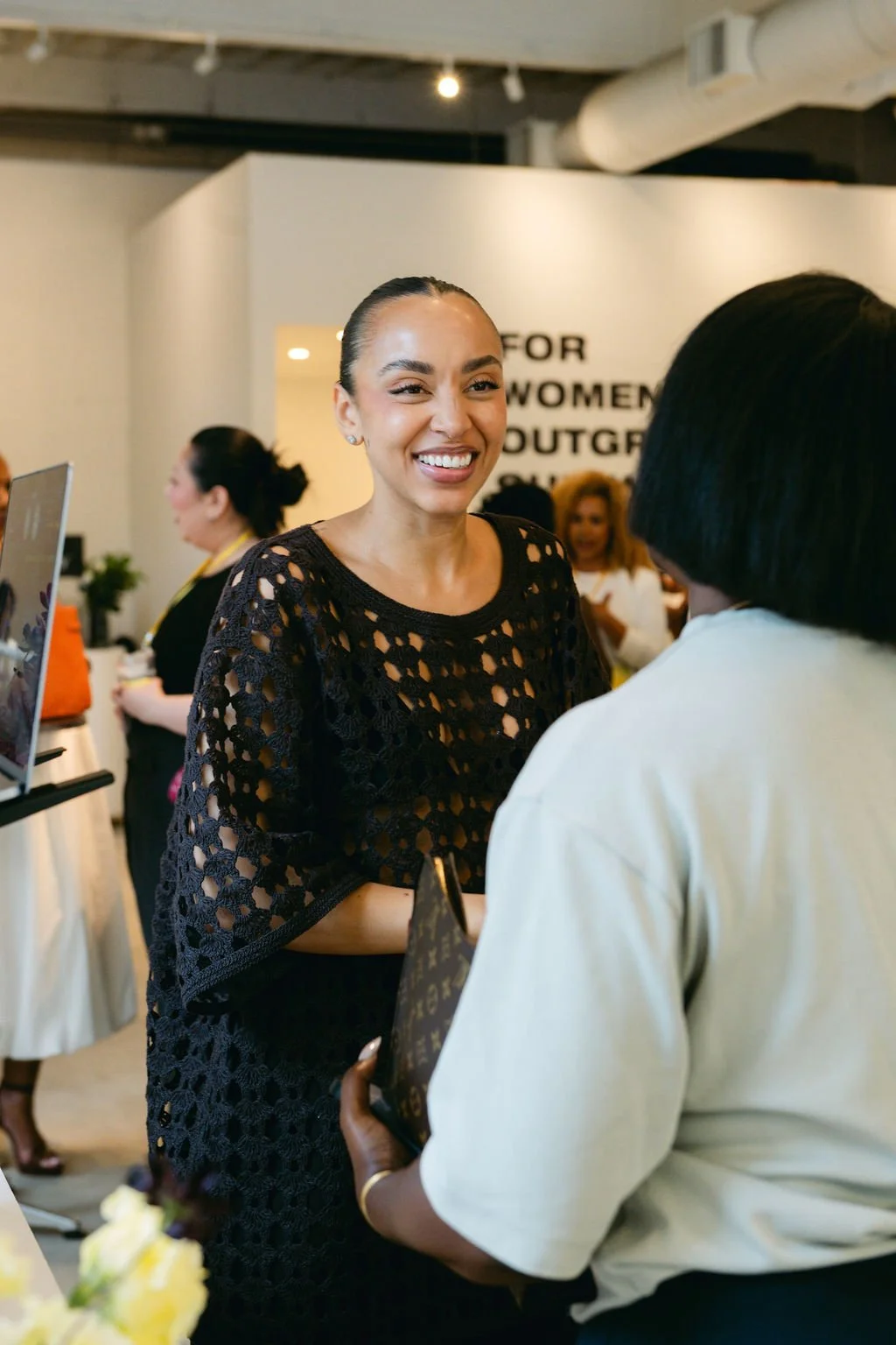 Women engaging in conversation at an indoor event, with smile on one woman's face.