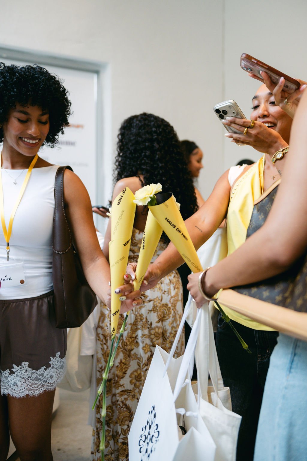 Women exchanging flowers and taking photos at an indoor event.
