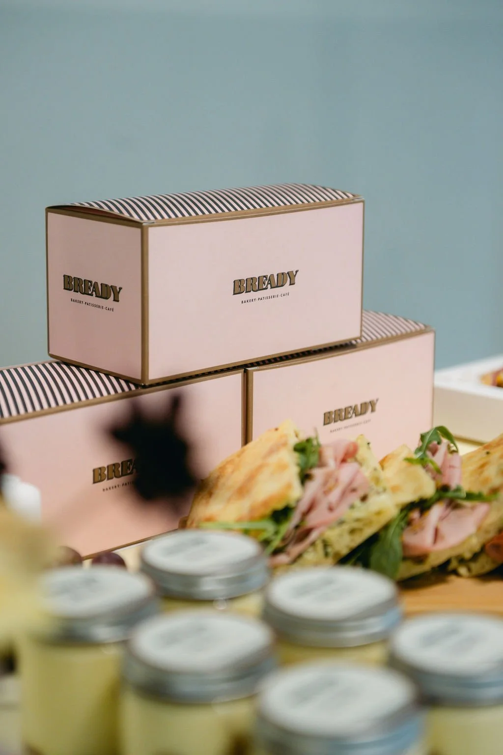 Boxes labeled 'BREADY' on a table, with sandwiches and small jars in the foreground.