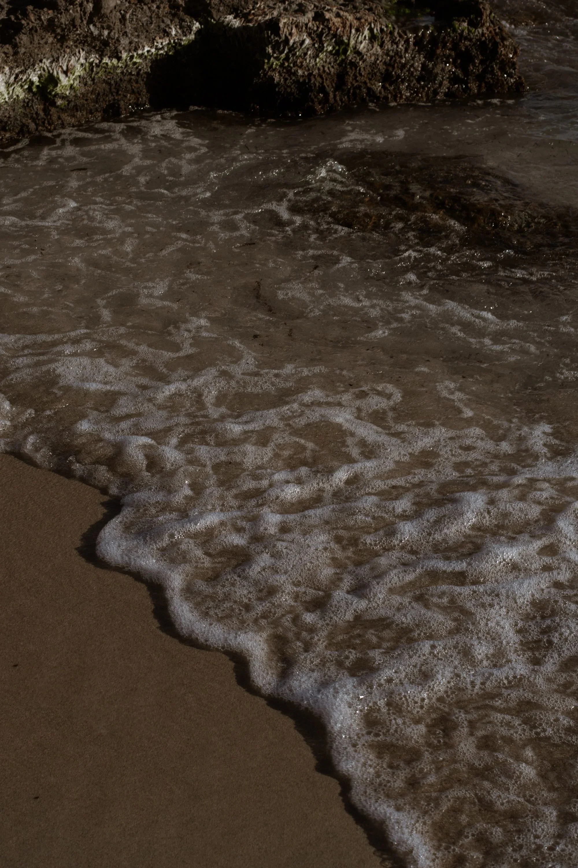 Foamy waves washing onto a sandy beach at night.