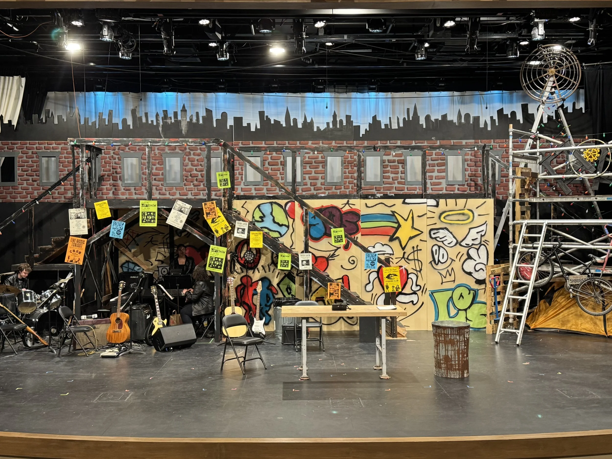 Stage with musical instruments, graffiti artwork, and construction scaffolding, indicating a rehearsal or set for a performance or show.