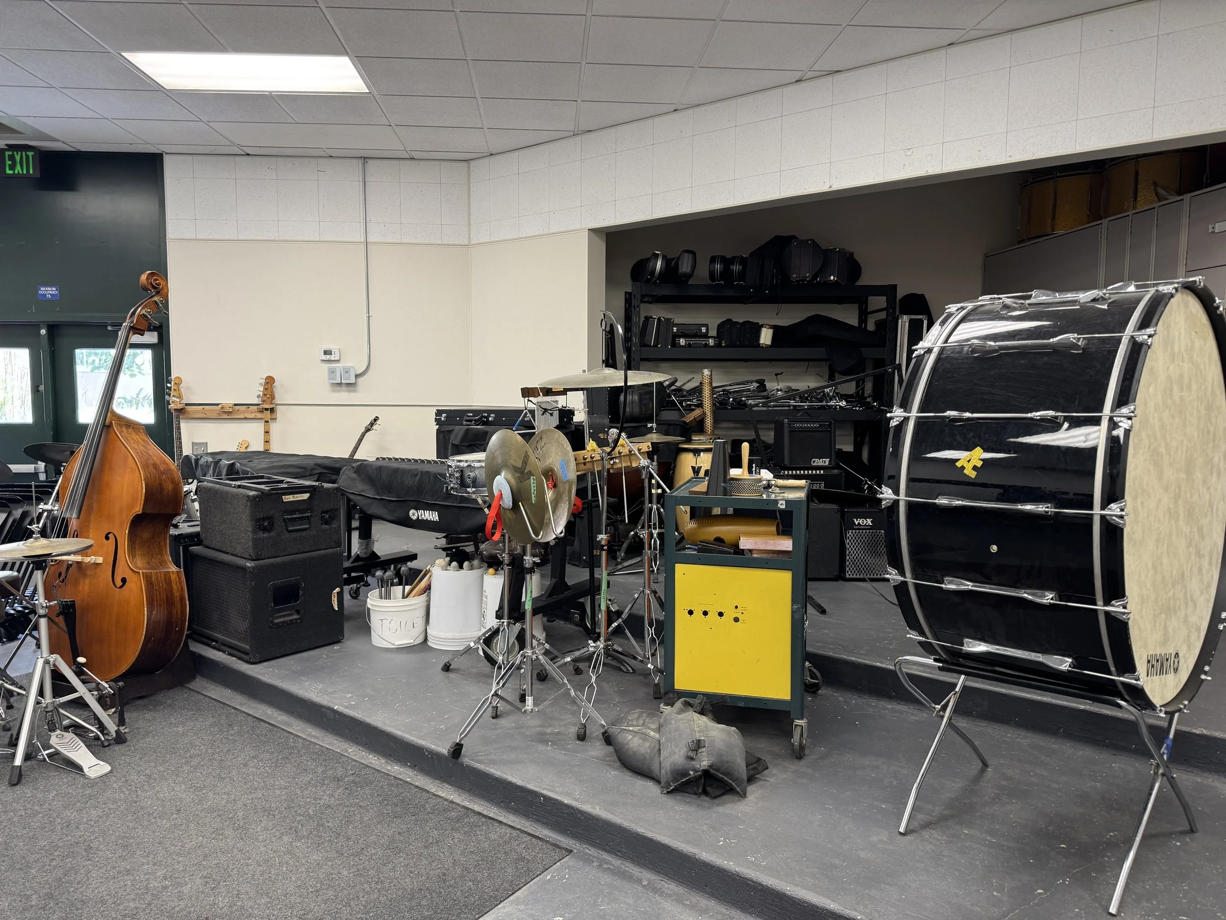 Room filled with musical equipment including drums, guitars, amps, and speakers, with shelves holding more gear and various musical accessories.