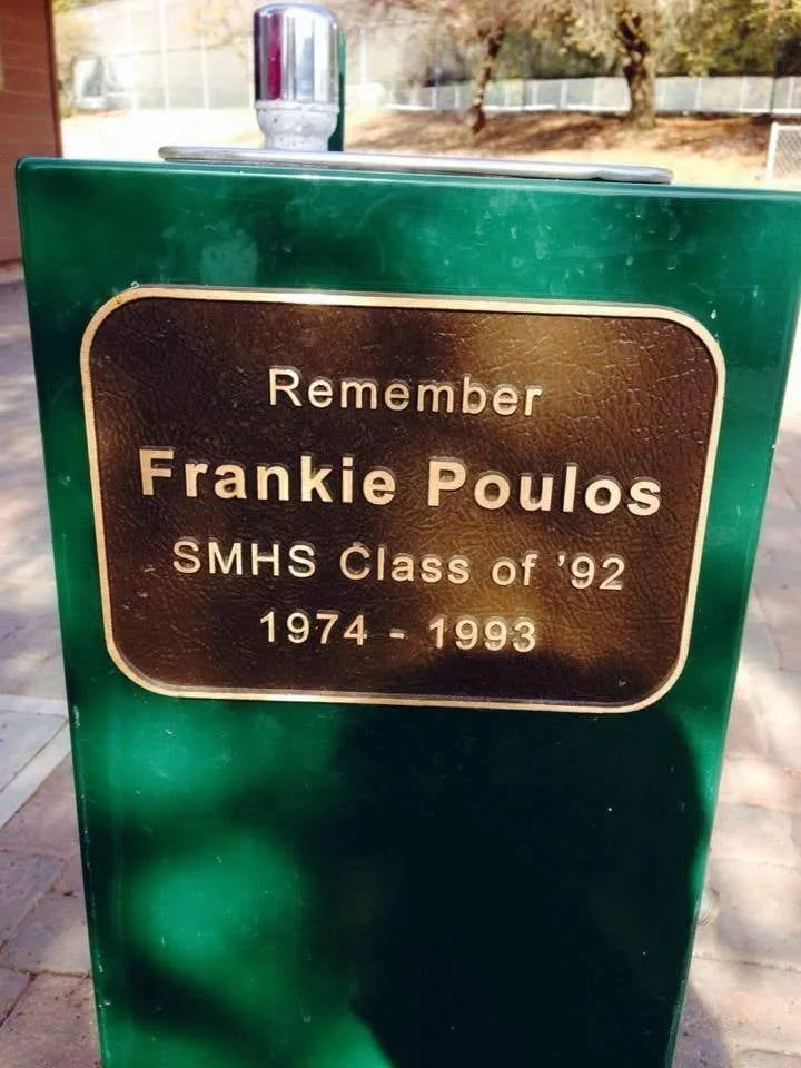 A green memorial monument with a brass plaque reminding viewers to remember Frankie Poulos, a member of the SMHS Class of 1992, who lived from 1974 to 1993.