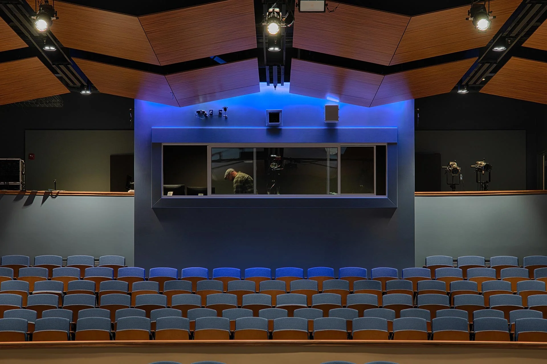 The Emily Gates Performing Arts Center stage and a glass window between the audience and the stage, a man is walking behind the glass.