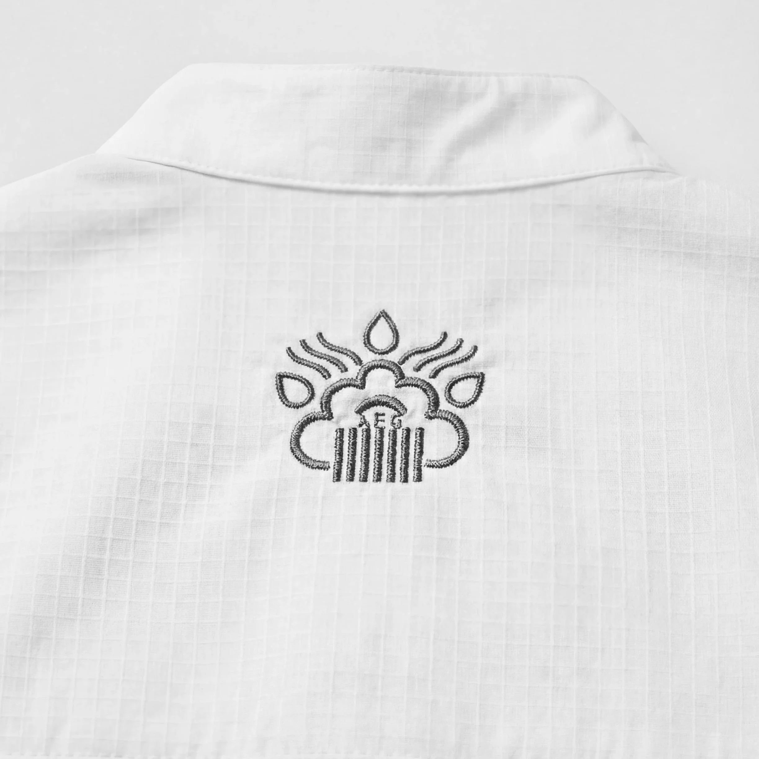 Close-up of white fabric with embroidered pattern featuring a sun and the word 'sun' beneath it.
