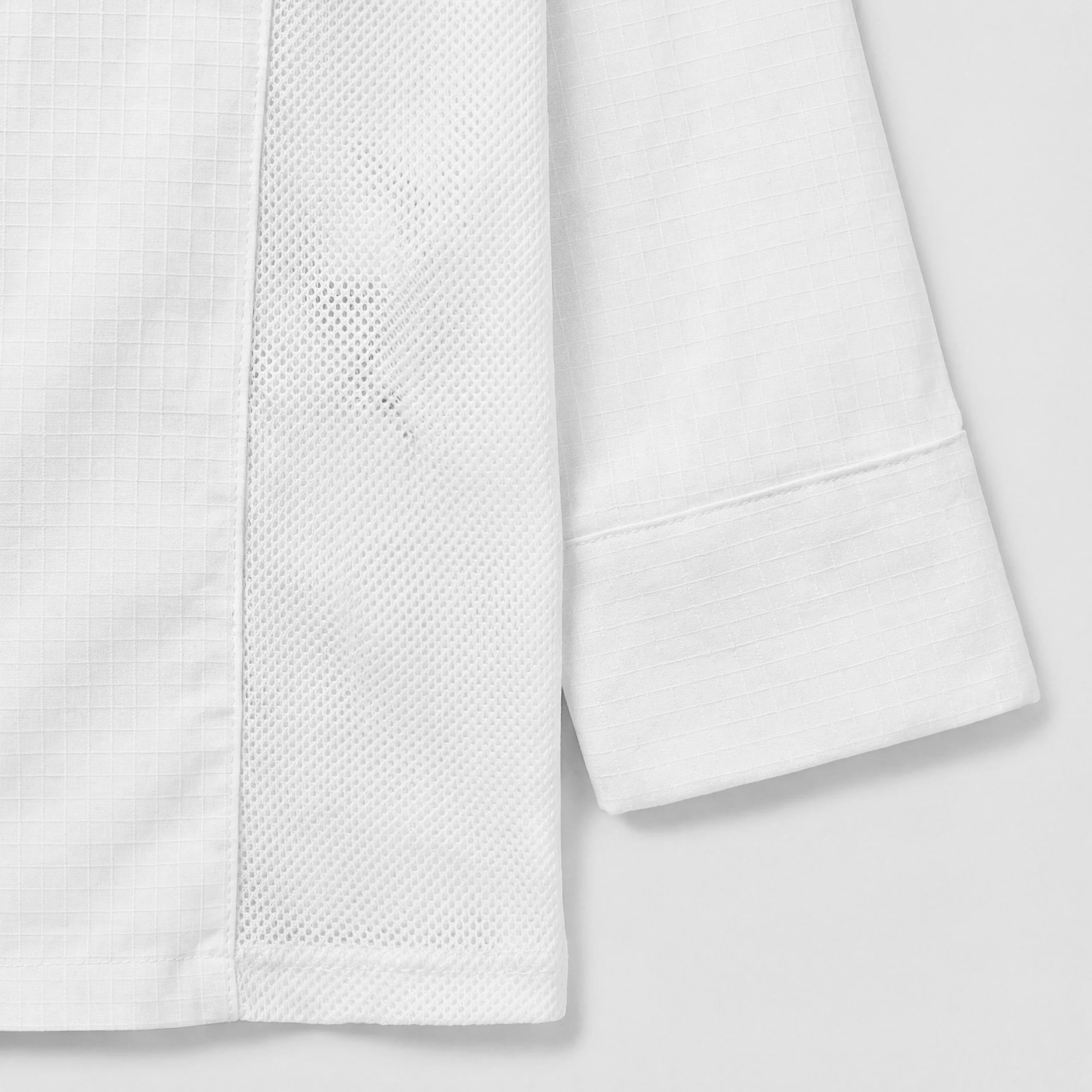 Close-up of white fabric with a textured grid pattern and a piece of mesh fabric, folded and layered.