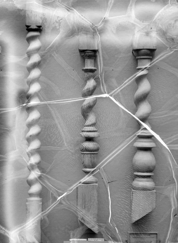 Four old wooden balusters or spindles behind a cracked and tattered plastic sheet.