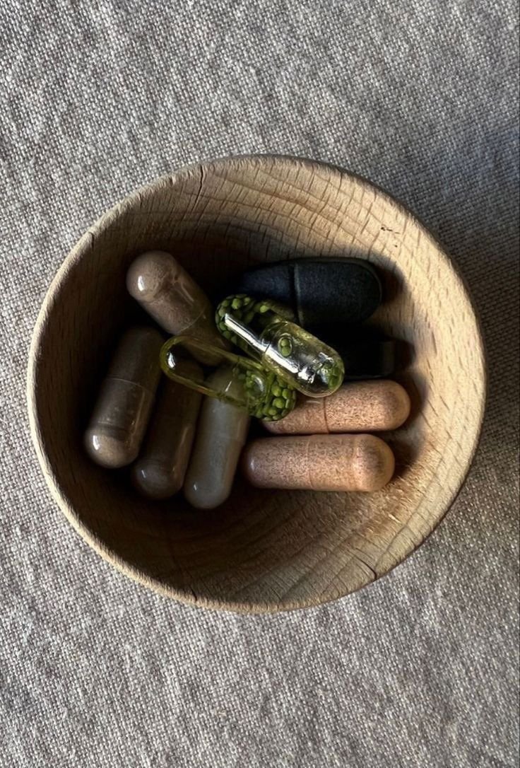 A wooden bowl containing assorted capsules and tablets on a textured gray fabric surface.