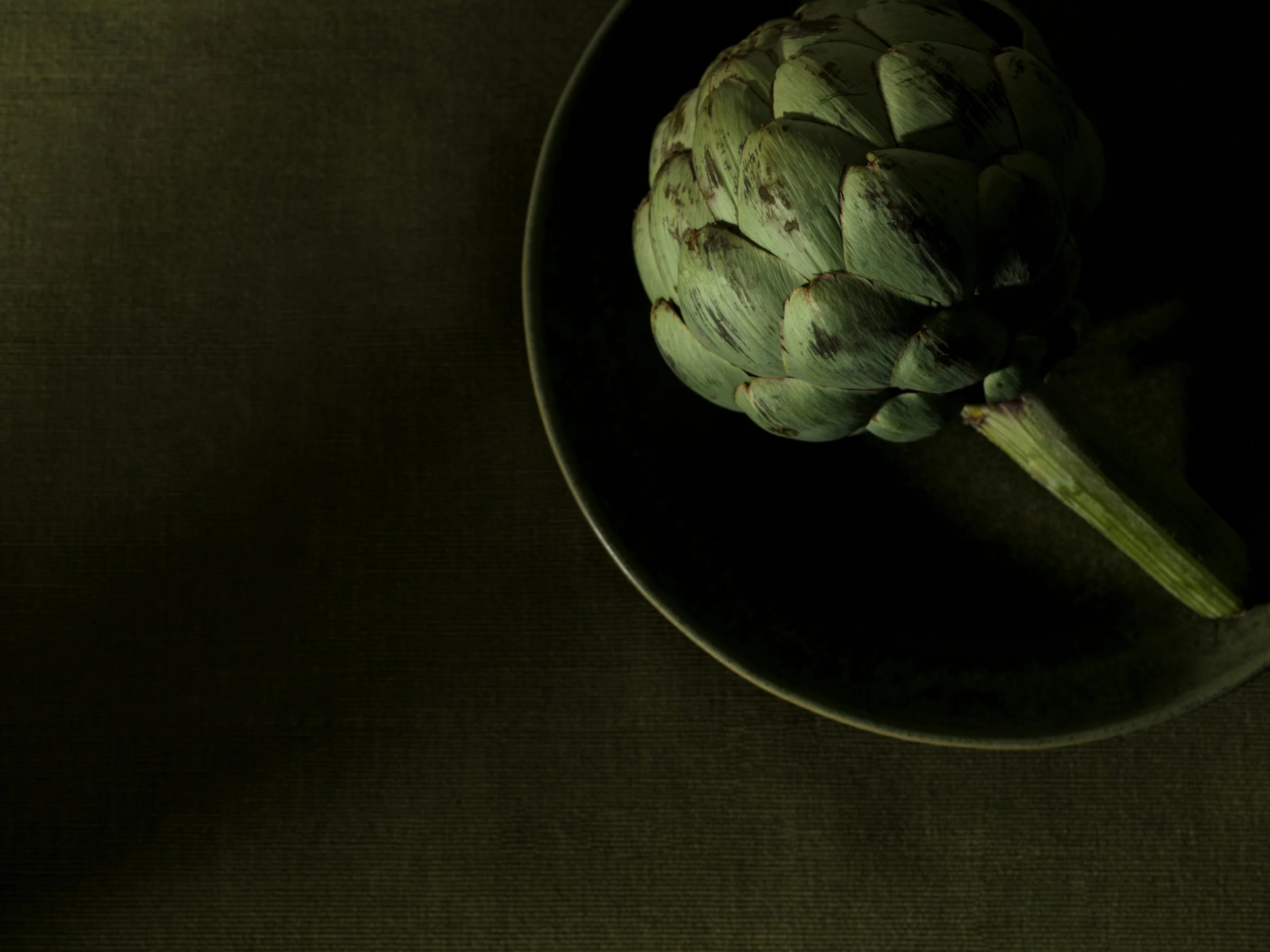 A peeled artichoke in a bowl, with dark lighting and background.