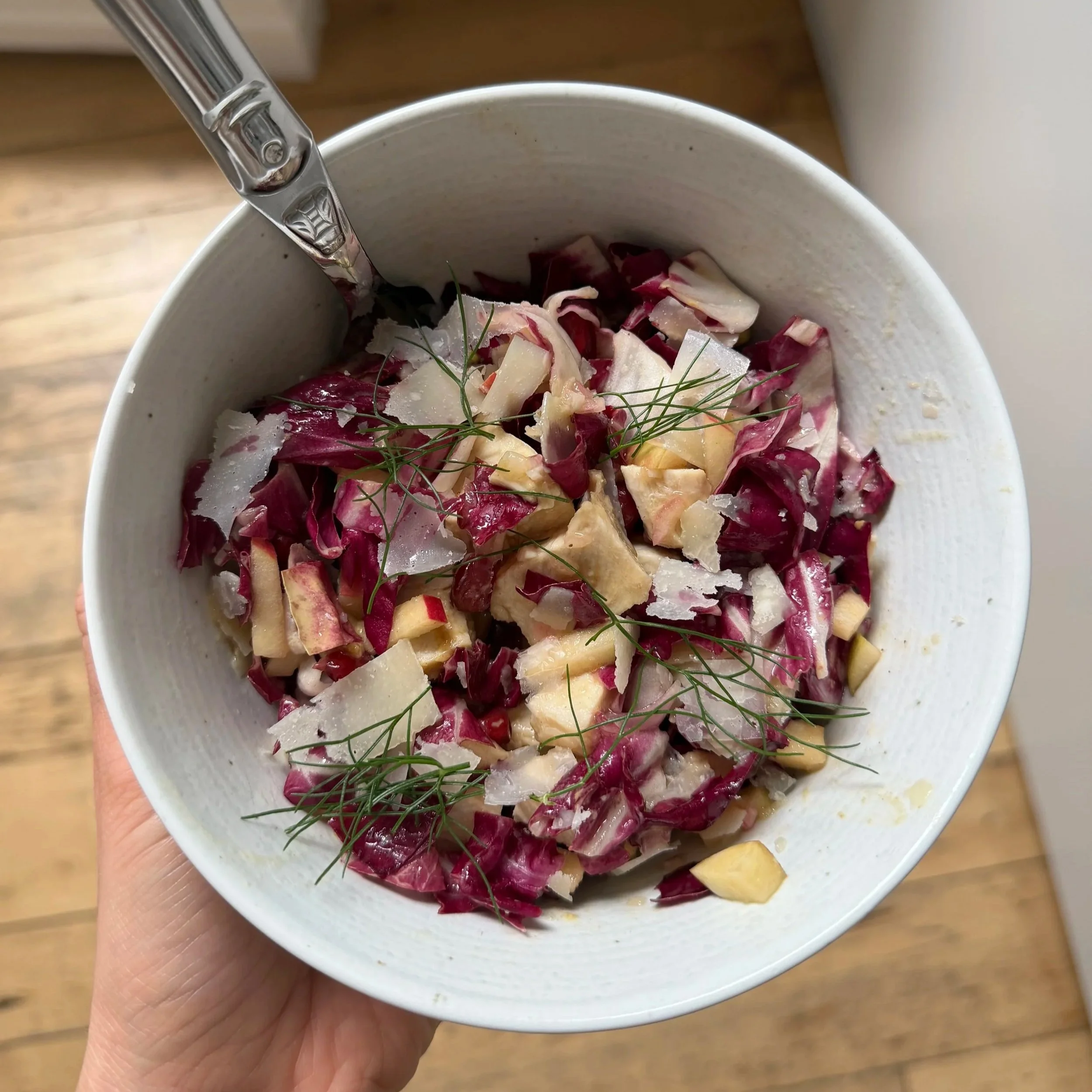 A bowl of chopped radicchio, cheese shavings, and fresh herbs, held in a person's hand.