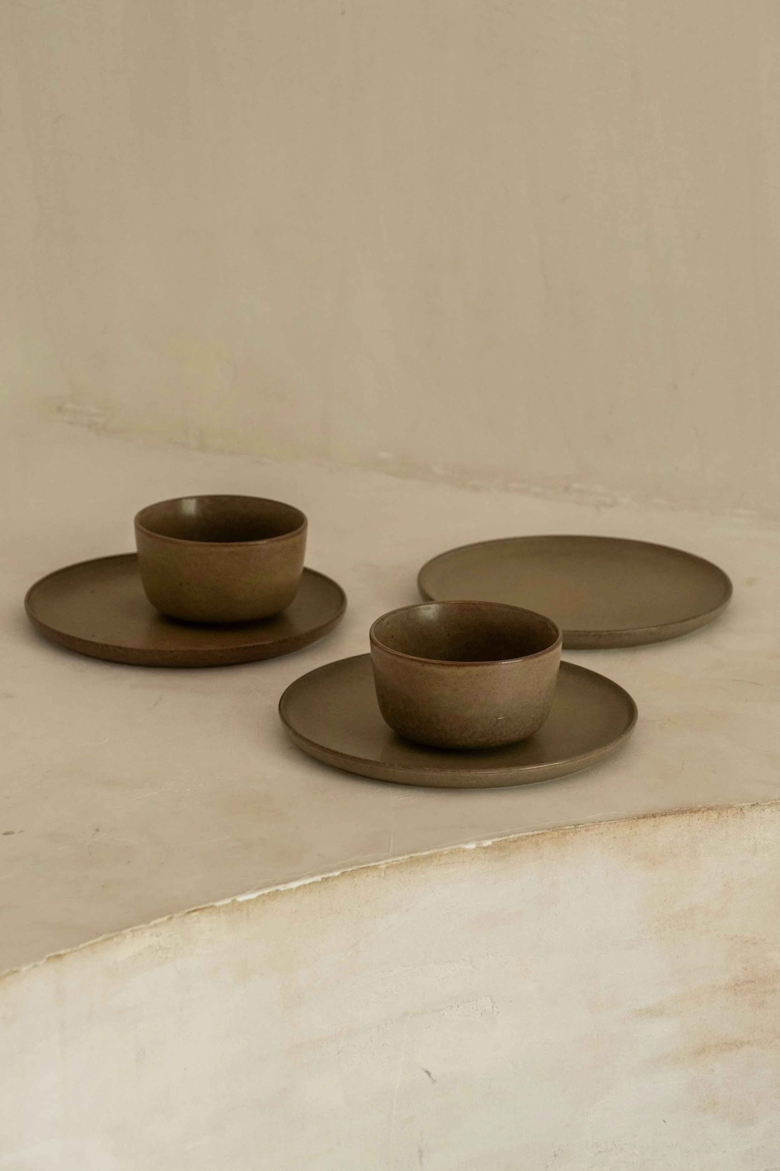 Brown ceramic cups and trays arranged on a table with a plain wall in the background.