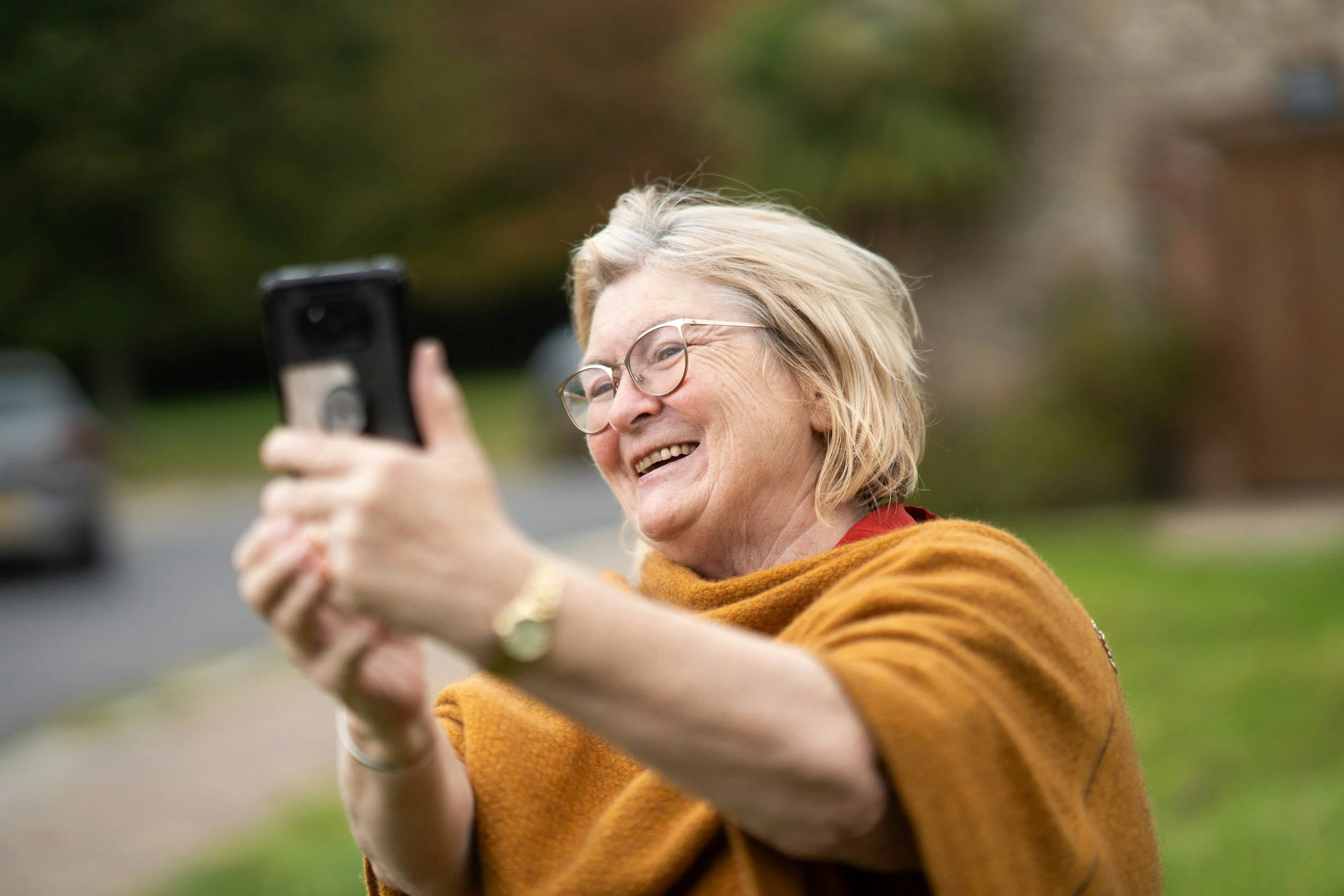 Older woman smiling while talking to family on cell phone, most likely on a video call.