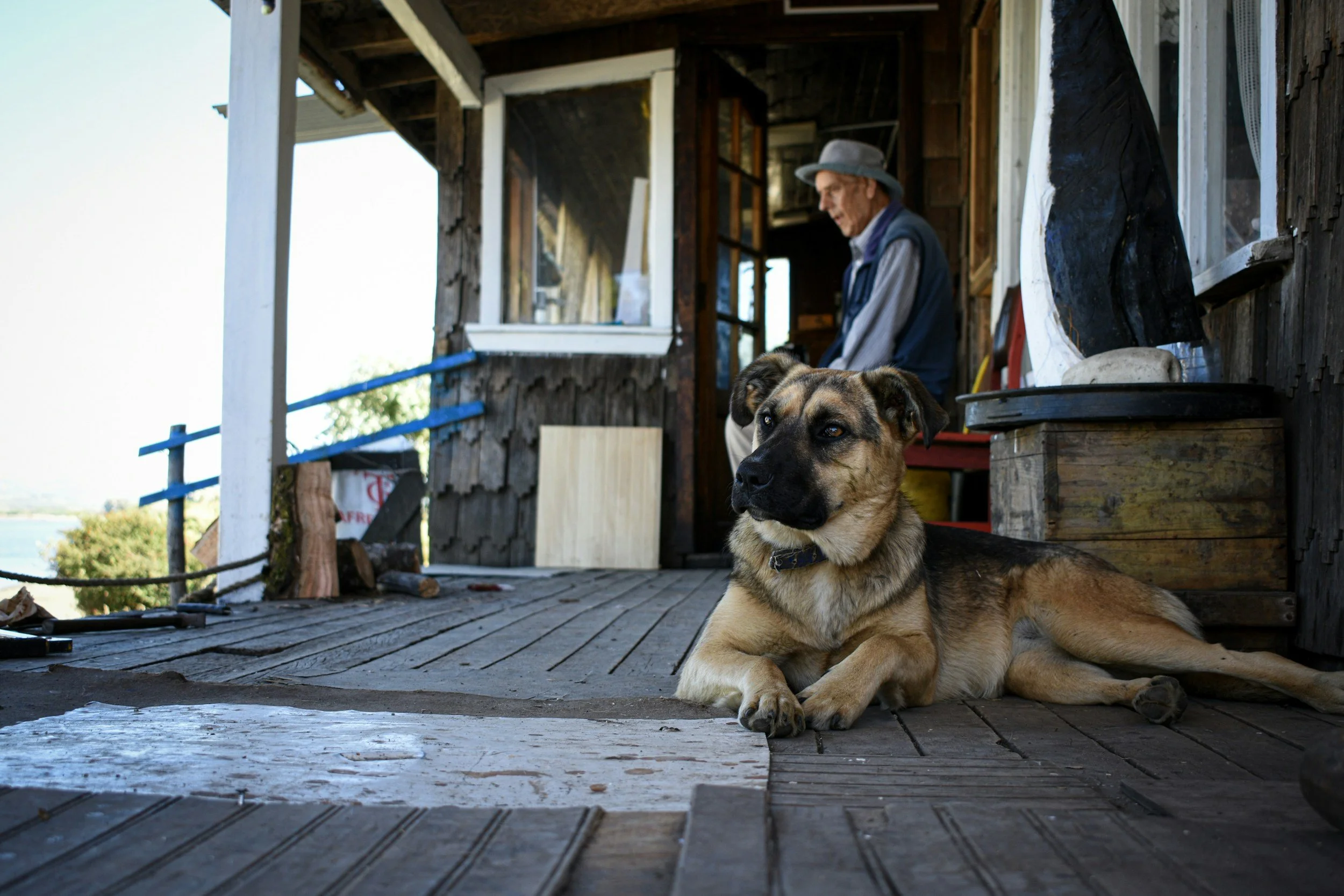 Elderly gentlemen wearing a fishin cap, sitting on his porch with his dog.