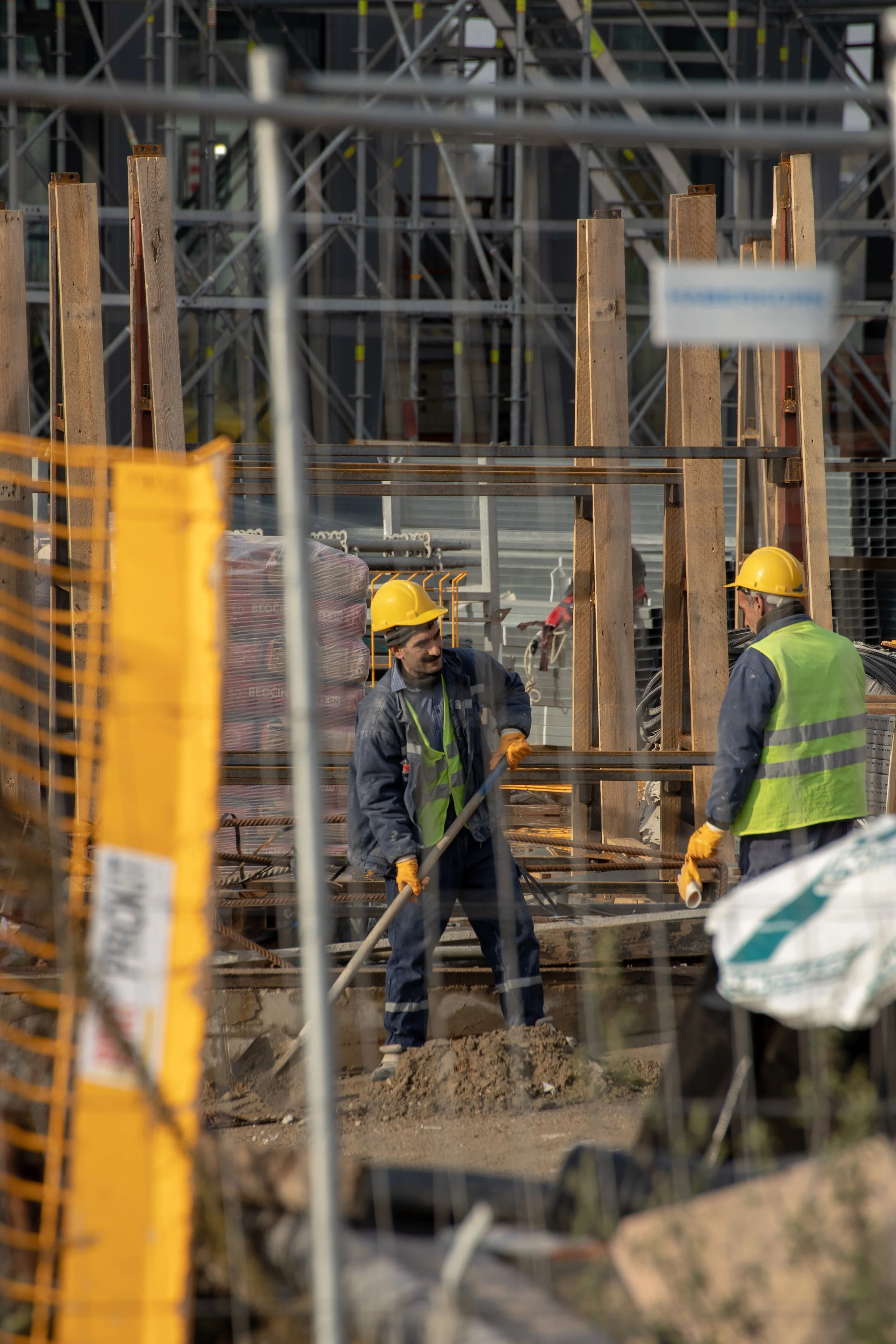 Construction workers wearing yellow hard hats and safety vests working on a construction site with scaffolding and building materials.