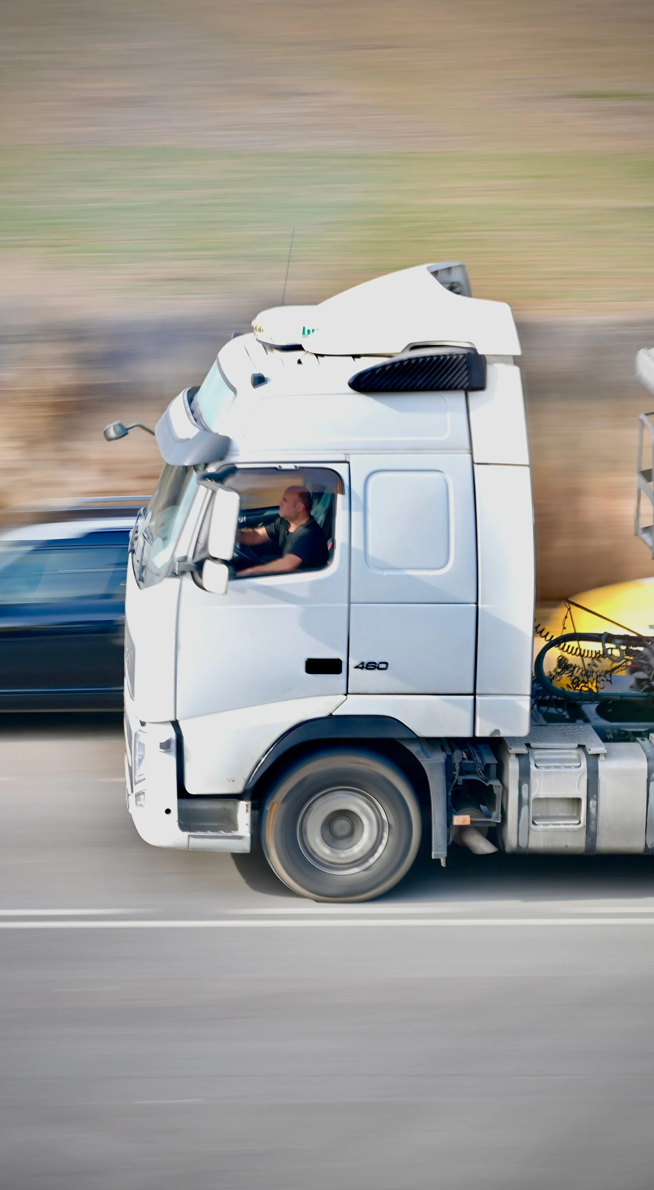 A white semi-truck driving on a highway with a blurred background, suggesting high speed, and a piece of equipment attached to the back.