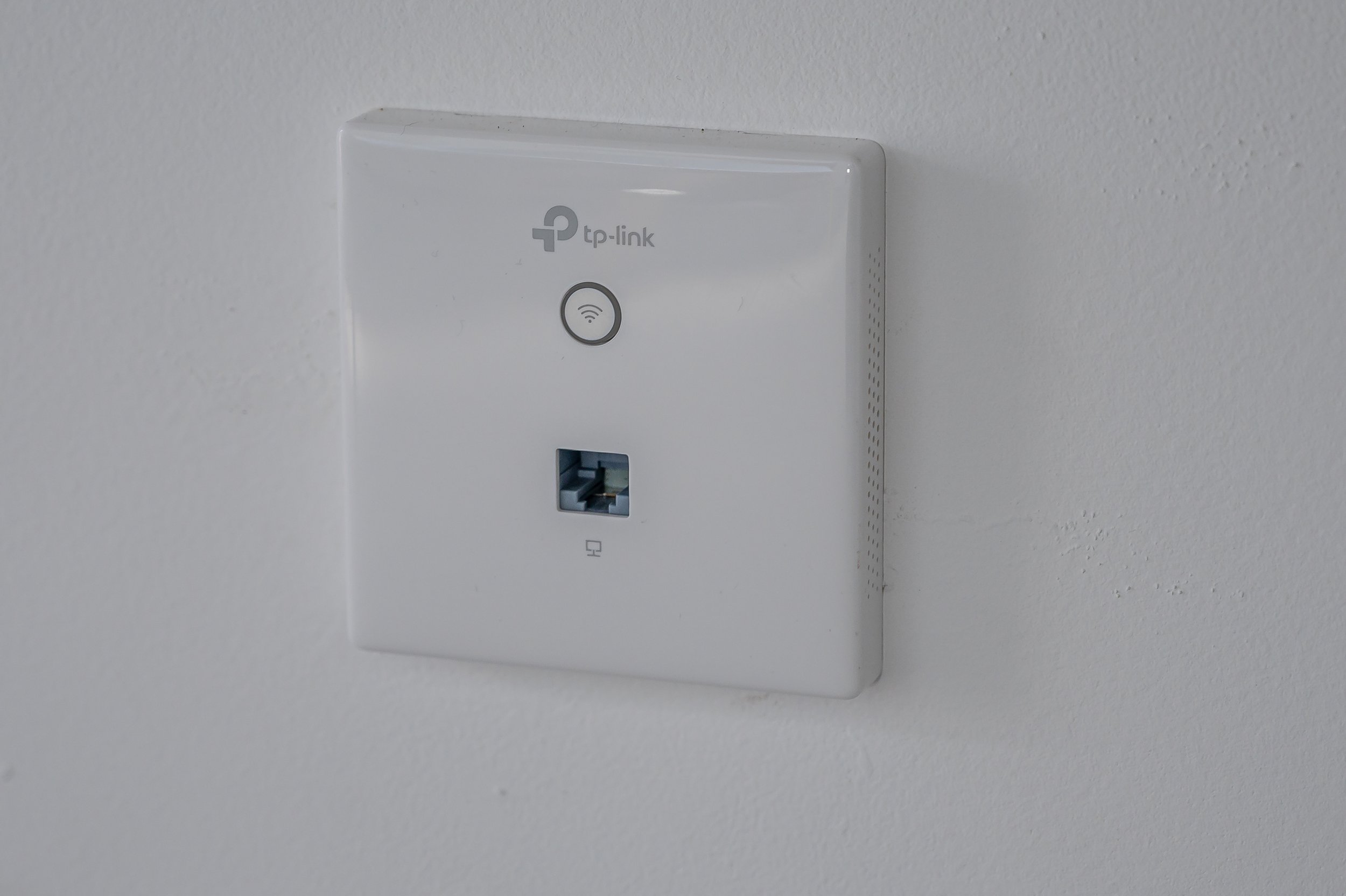 Wall-mounted TP-Link Wi-Fi mesh router with an Ethernet port beneath it, installed on a plain white wall.