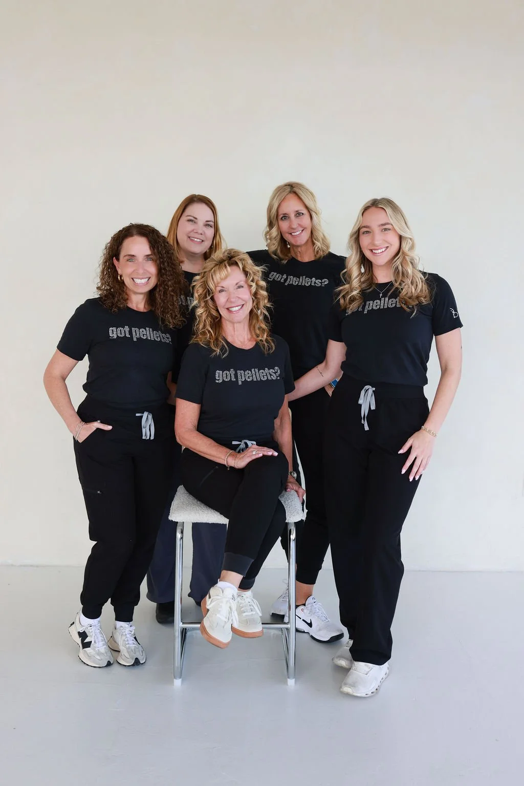 Group of five women wearing matching black T-shirts with 'got pellets?' text, posing together indoors against a plain white wall.