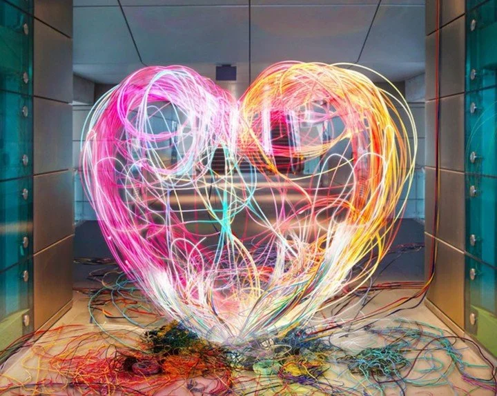 A mass of old cables come together to form a glowing neon heart shape. 
