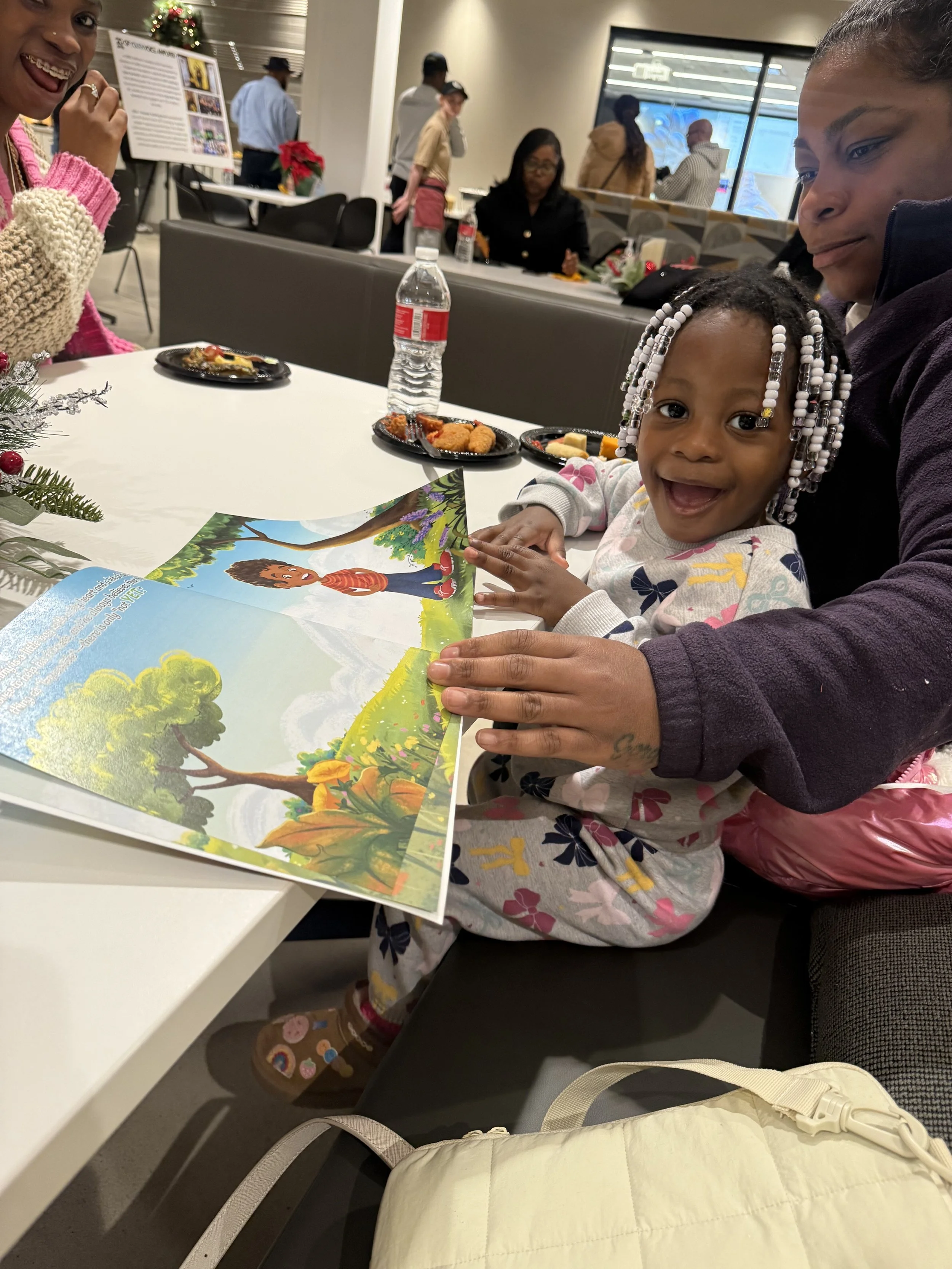 A young girl with braided hair, decorated with beads, smiling widely and holding a colorful illustrated picture book named Tommy's Magic Word: Yet