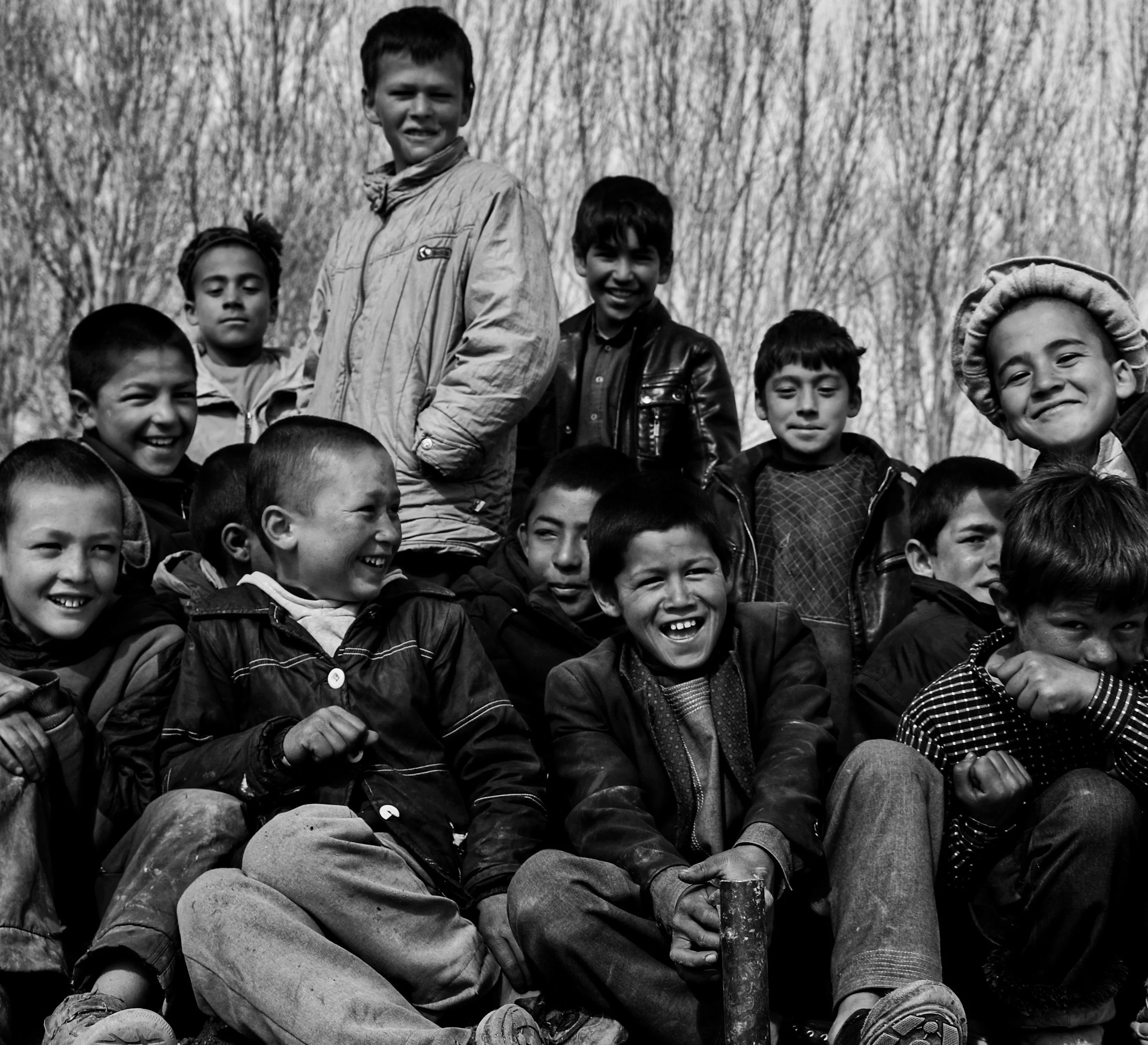 Group of children smiling and sitting outdoors in front of trees.