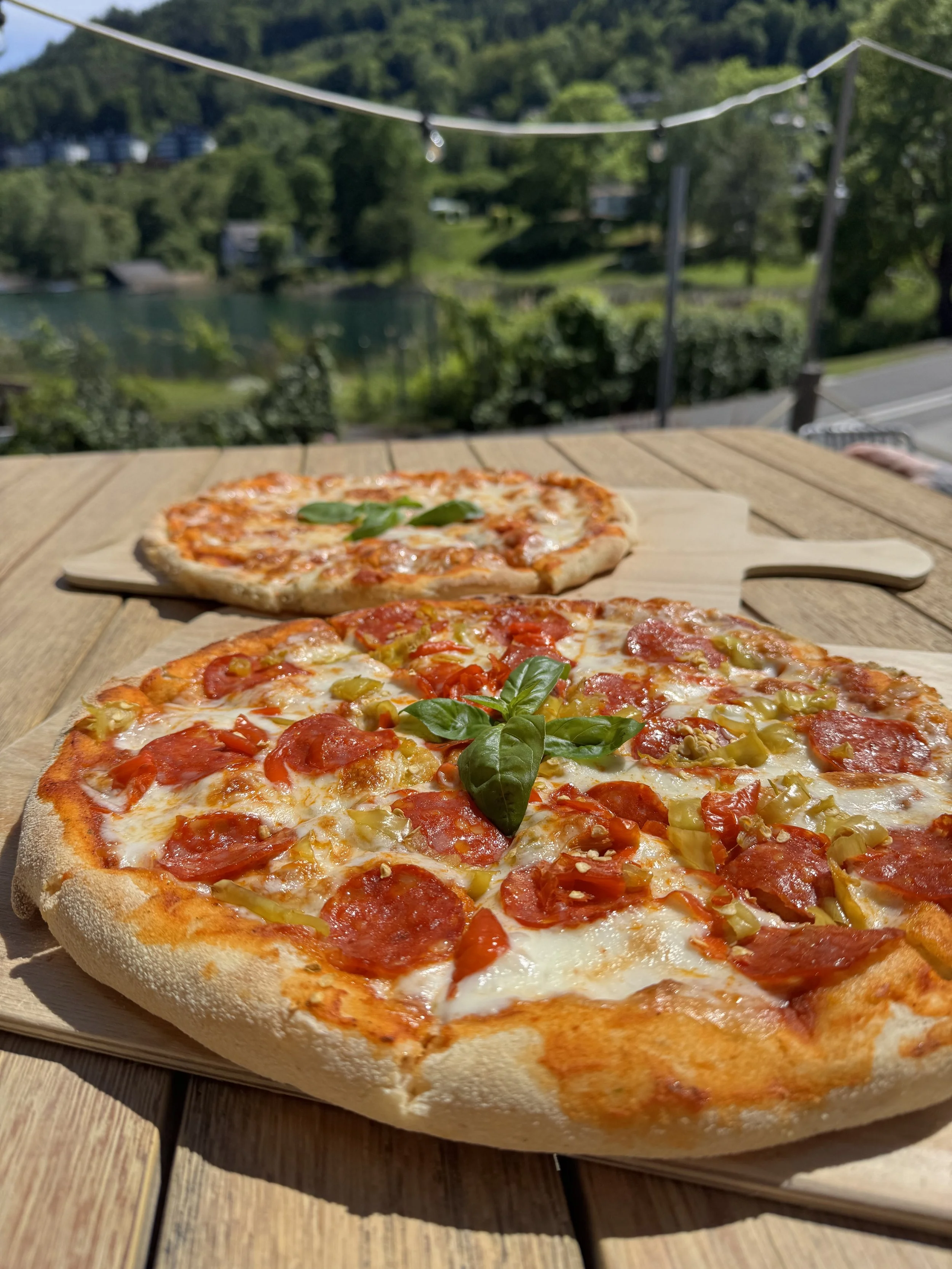 Pizzastücke mit Tomaten, Fleisch und Basilikum auf einer Holzplatte im Freien.