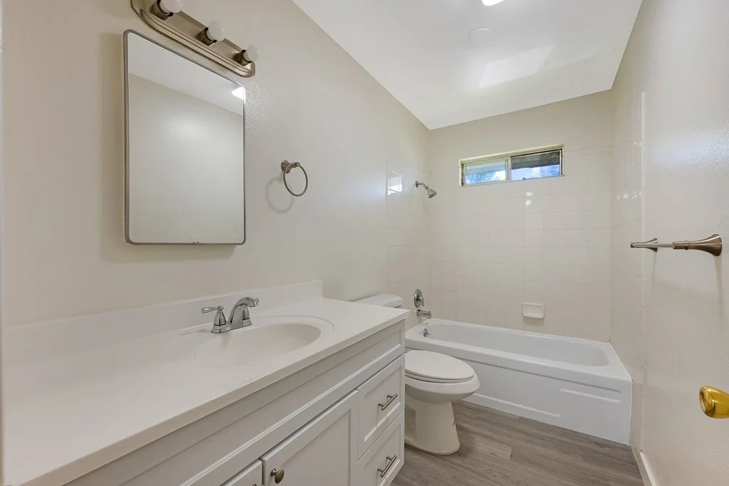 Bathroom with a white vanity, mirror, towel ring, toilet, bathtub, small high window, and a towel bar on the wall.