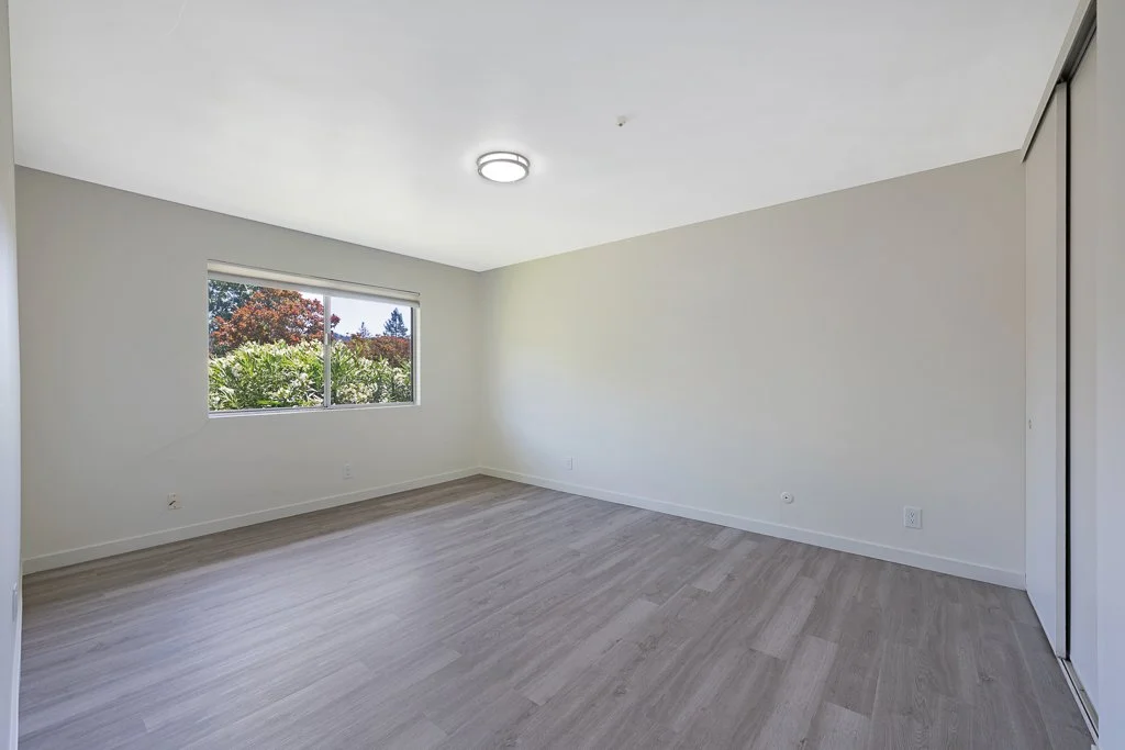 Empty room with white walls, a window overlooking greenery, and a closet with sliding doors.