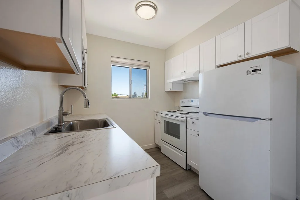 Small kitchen with white cabinets, a white refrigerator, a white stove, a single window, and a marble countertop.
