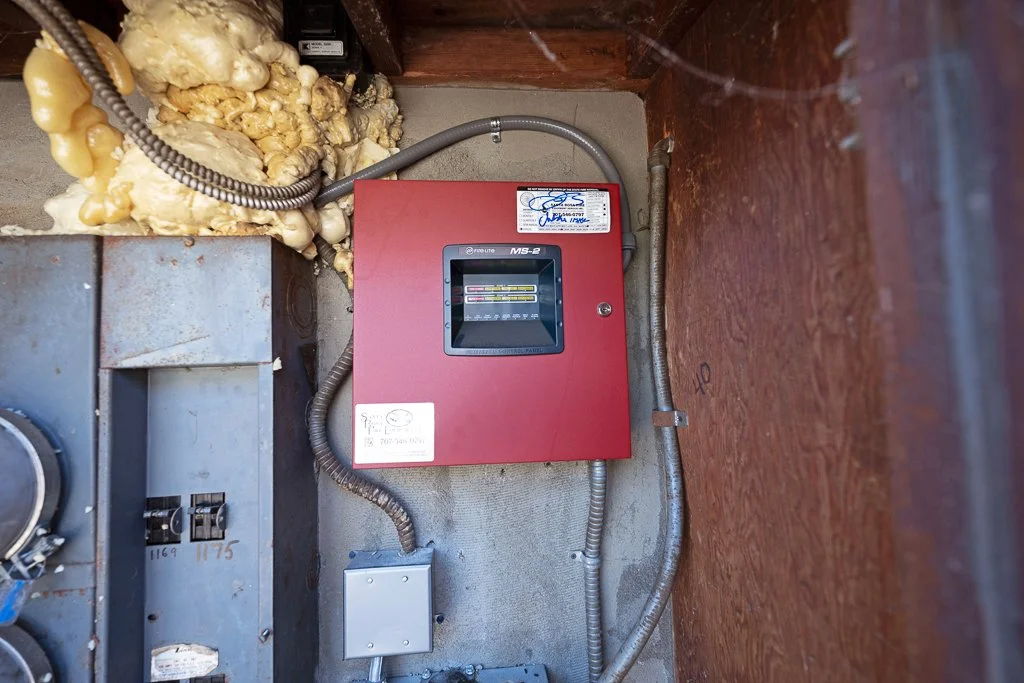 Electrical panel mounted on a wall with exposed insulation and wiring nearby.