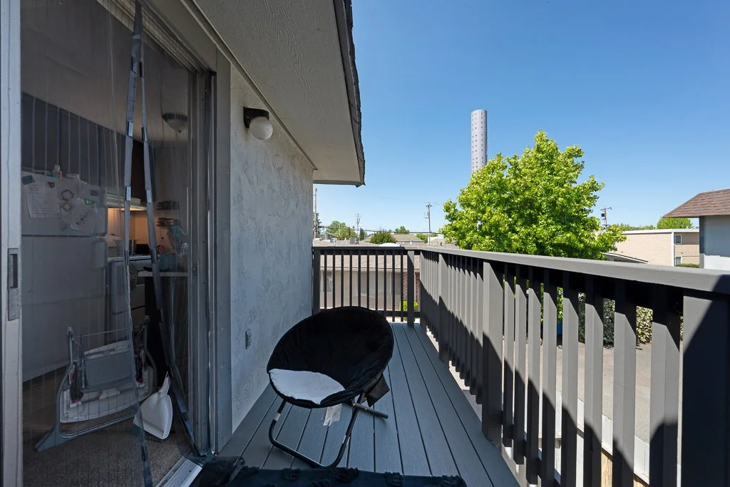 Balcony with a black chair, railing, and view of a tree and clear blue sky.