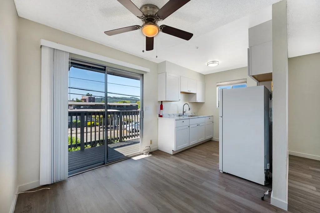 Bright, open kitchen and dining area with sliding glass door leading to a balcony, white cabinets, a refrigerator, and wood-like flooring.