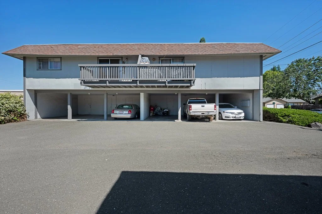 Two-story residential building with a parking area underneath, with four cars parked in the spaces.