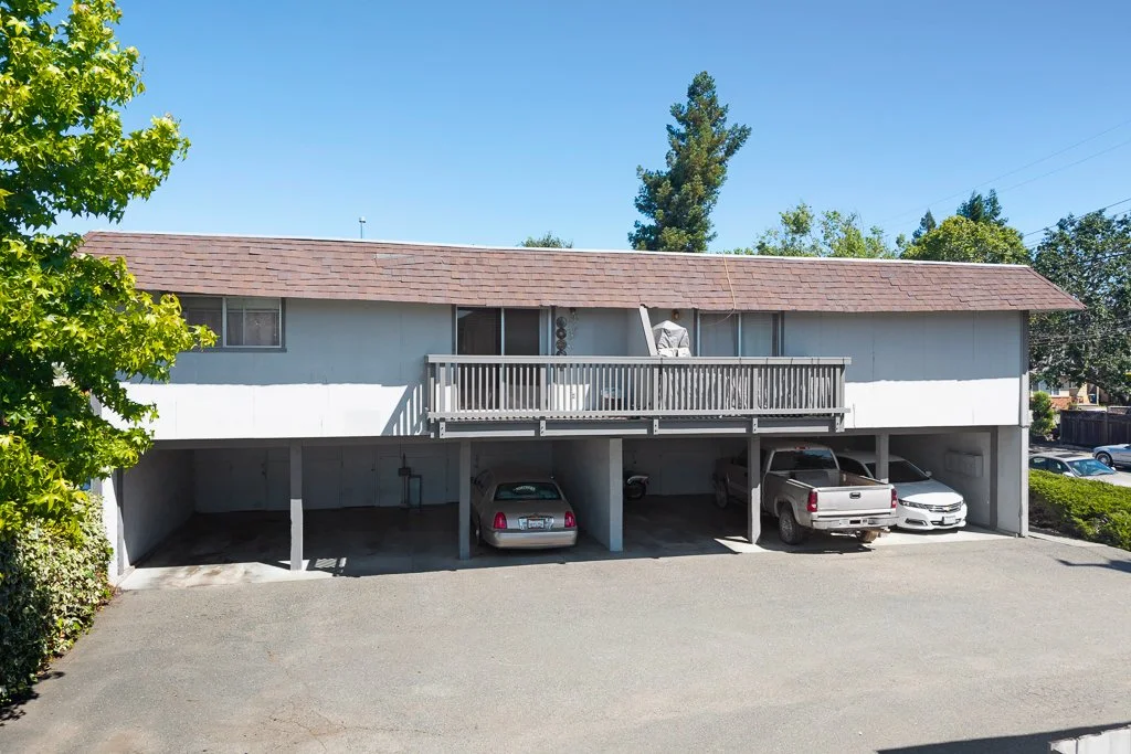 Parking garage with three parked vehicles underneath an apartment building with a balcony.