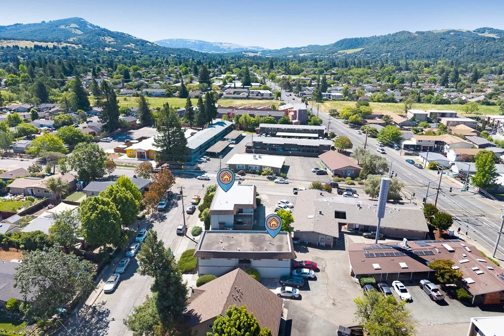 Aerial view of a small town with residential neighborhoods, commercial buildings, and a hillside in the background under a clear blue sky.