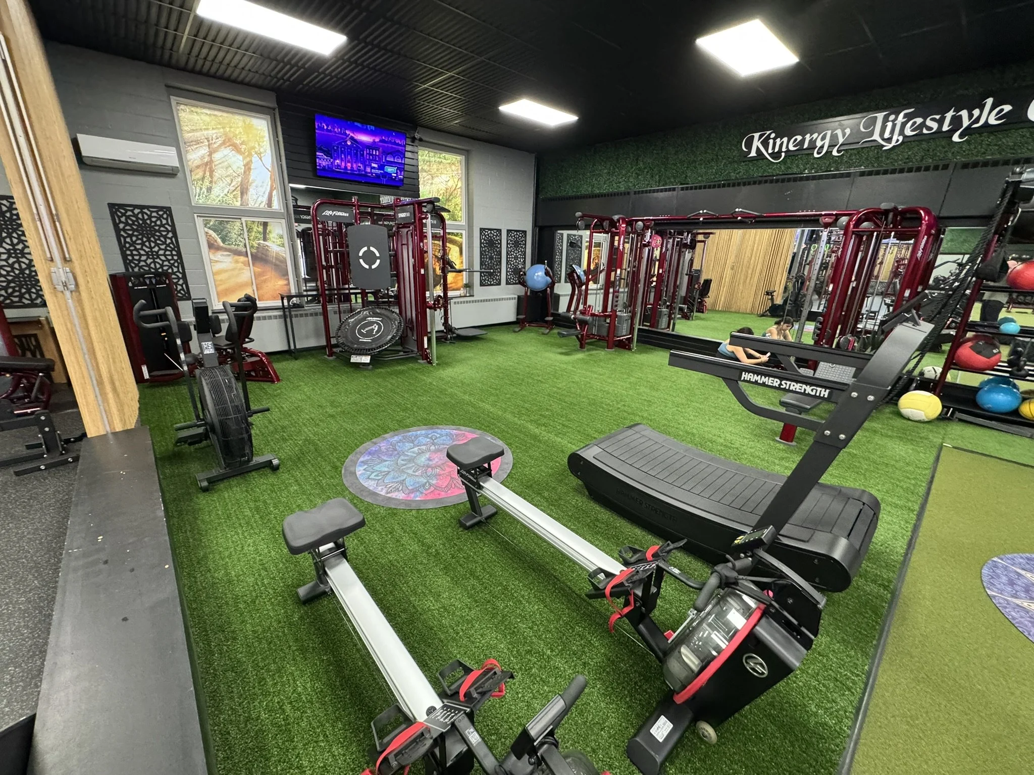 Gym with various exercise equipment, artificial turf flooring, motivational poster, and a television, with 