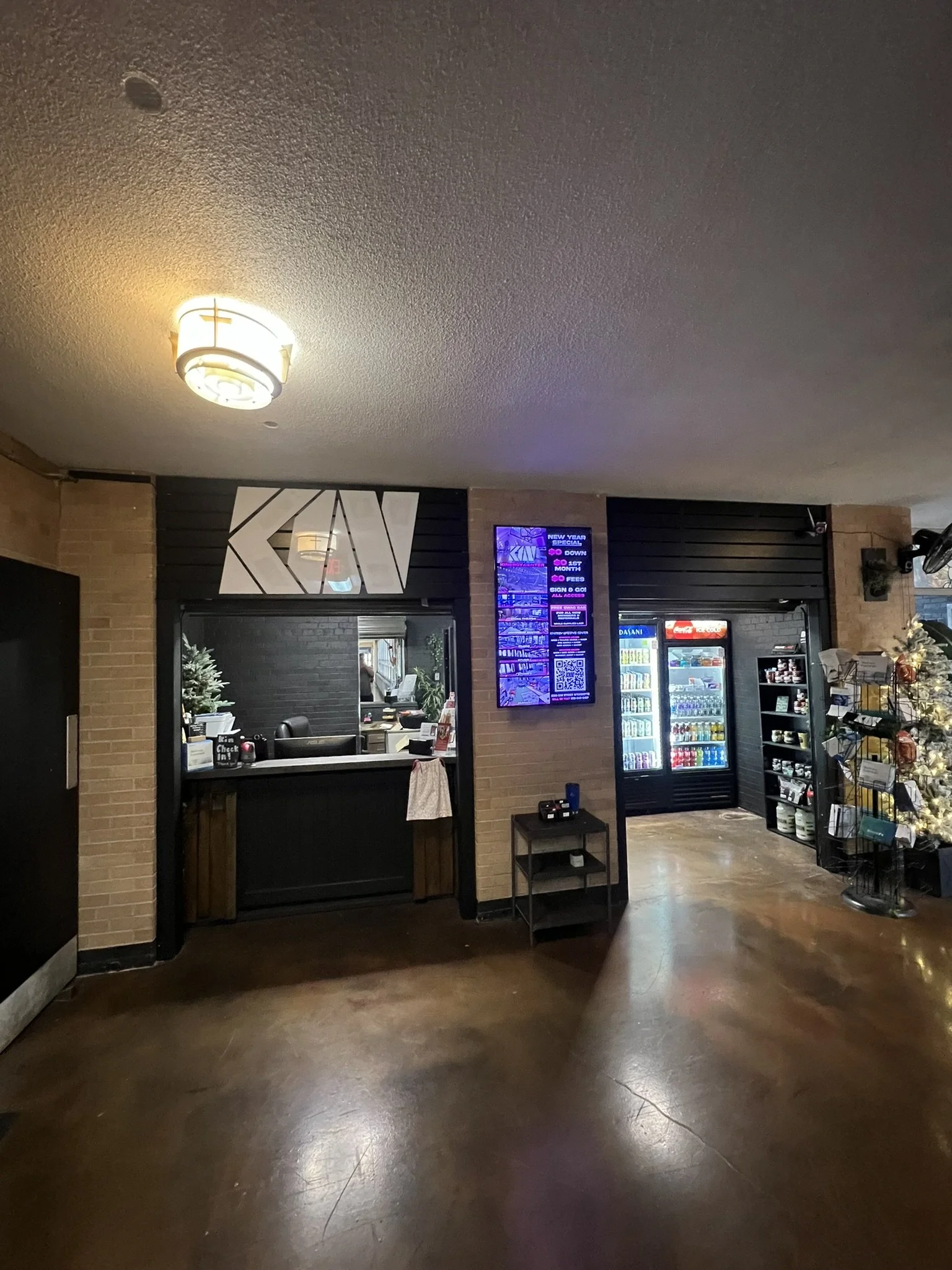 A reception area with a black window counter, digital display, vending machines, and a Christmas tree on the right side.