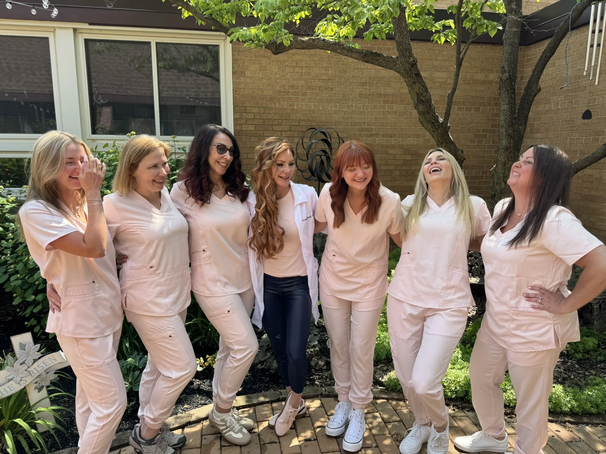 A group of women dressed in matching pink uniforms standing together outdoors, smiling and laughing.